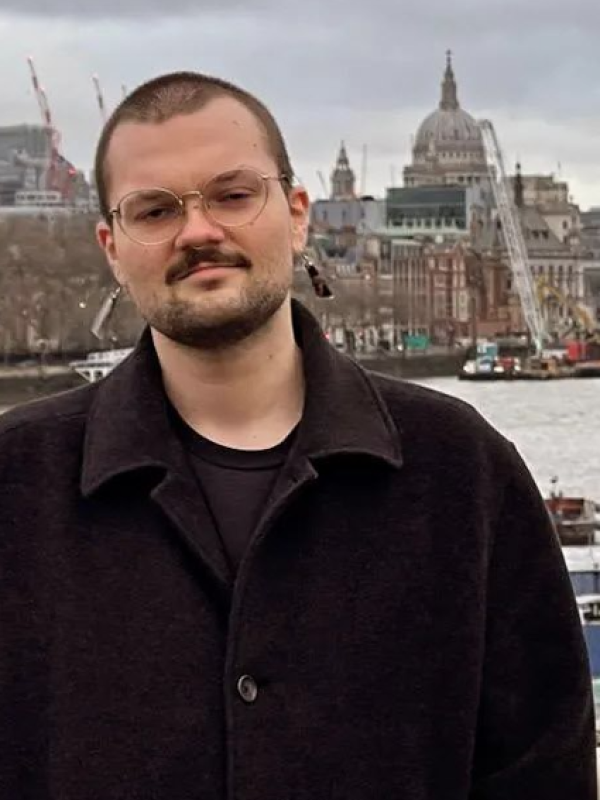 Jay Hadfield, a person with buzzed brown hair, a mustache, and glasses, standing in front of architecture.